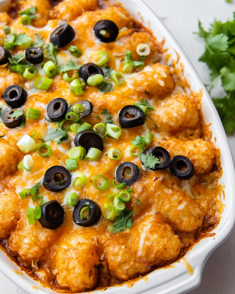 A dish of tater tots with cheese and black olives.