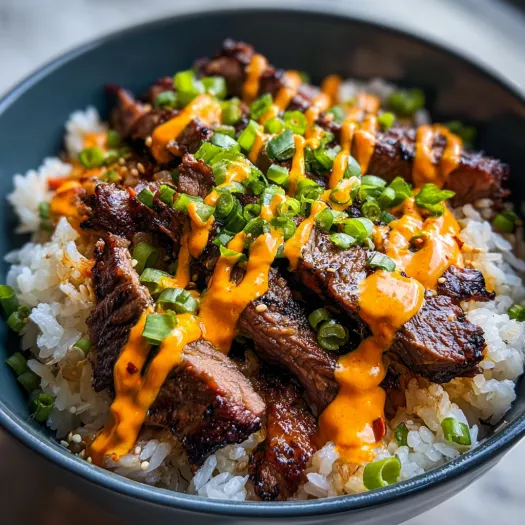 A bowl of meat and rice with a spicy cream drizzle.