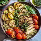 A bowl filled with chicken, tomatoes, spinach, and other goodies.