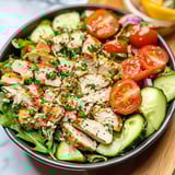 A bowl holding chopped chicken salad with colorful veggies like tomatoes, cucumbers, and peppers.