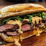 A steak sandwich loaded with veggies and creamy garlic sauce.