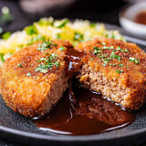 Menchi Katsu (Japanese ground meat cutlet) looking super crispy on a black tray, sauce on the side.