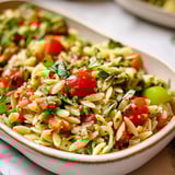 A bowl piled high with orzo, chickpeas, and fresh veggies.