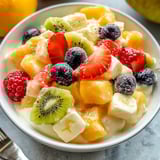 A bowl of fruit salad with vanilla pudding.