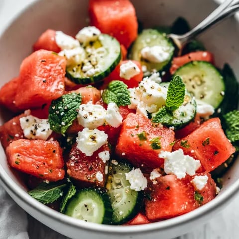 Big bowl filled with watermelon, cucumber, and feta, topped with fresh herbs.