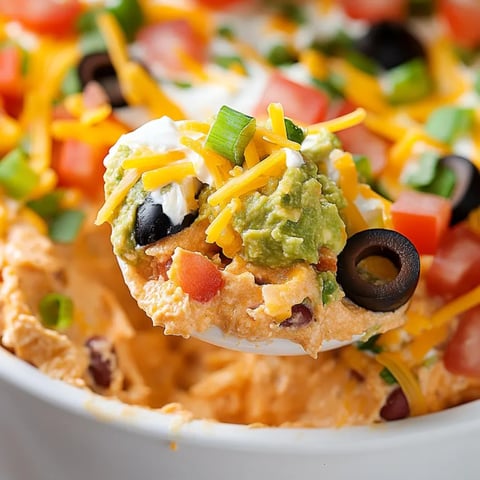 A big bowl of taco dip with a spoon hanging out.