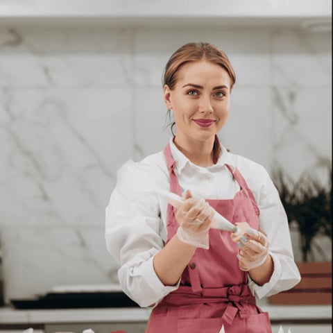 A woman in a pink apron is smiling.